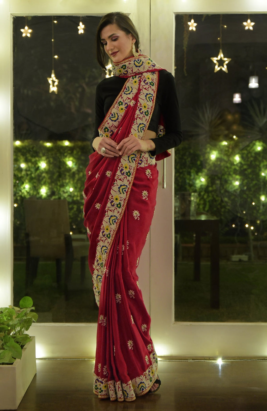 A woman models a red Parsi Gara hand-embroidered saree with a black blouse.