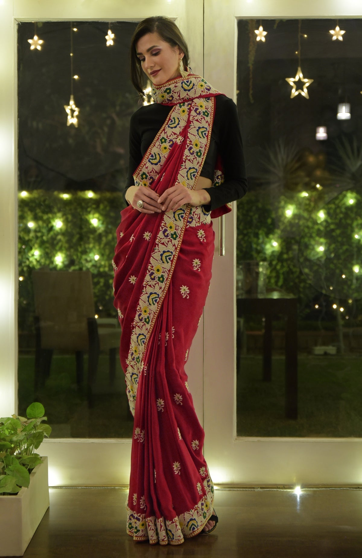 A woman models a red Parsi Gara hand-embroidered saree with a black blouse.