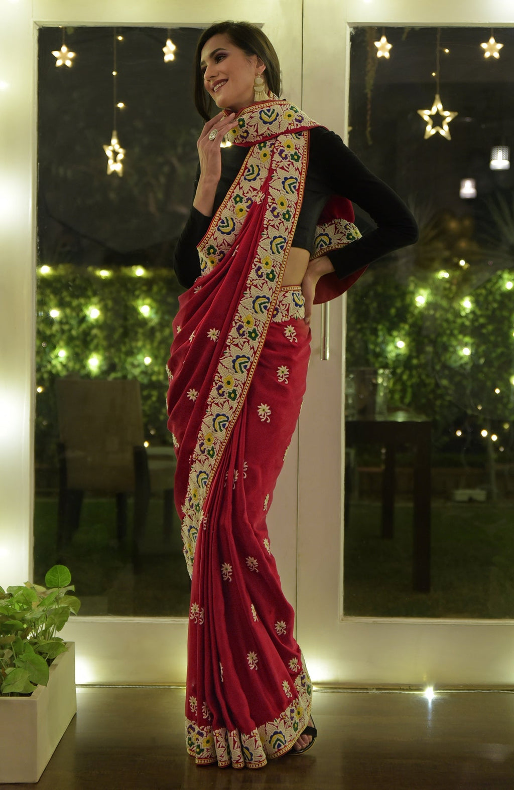 A woman models a red Parsi Gara hand-embroidered saree with a black blouse.
