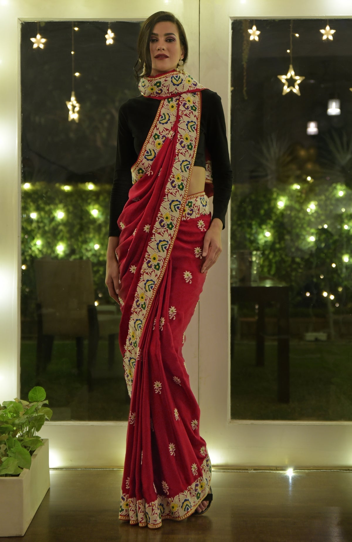 A woman models a red Parsi Gara hand-embroidered saree with a black blouse.