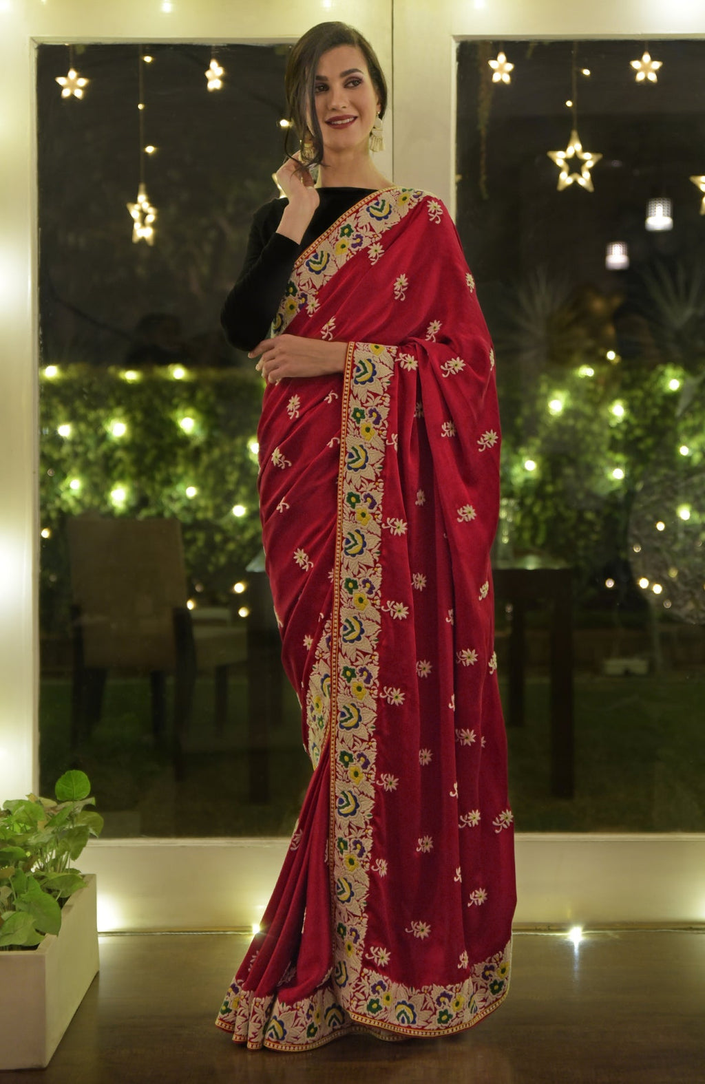 A woman models a red Parsi Gara hand-embroidered saree with a black blouse.