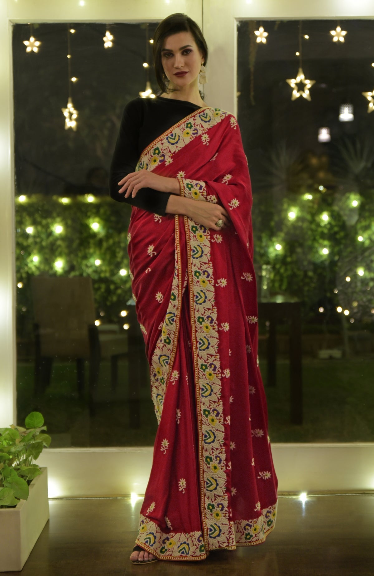 A woman models a red Parsi Gara hand-embroidered saree with a black blouse.