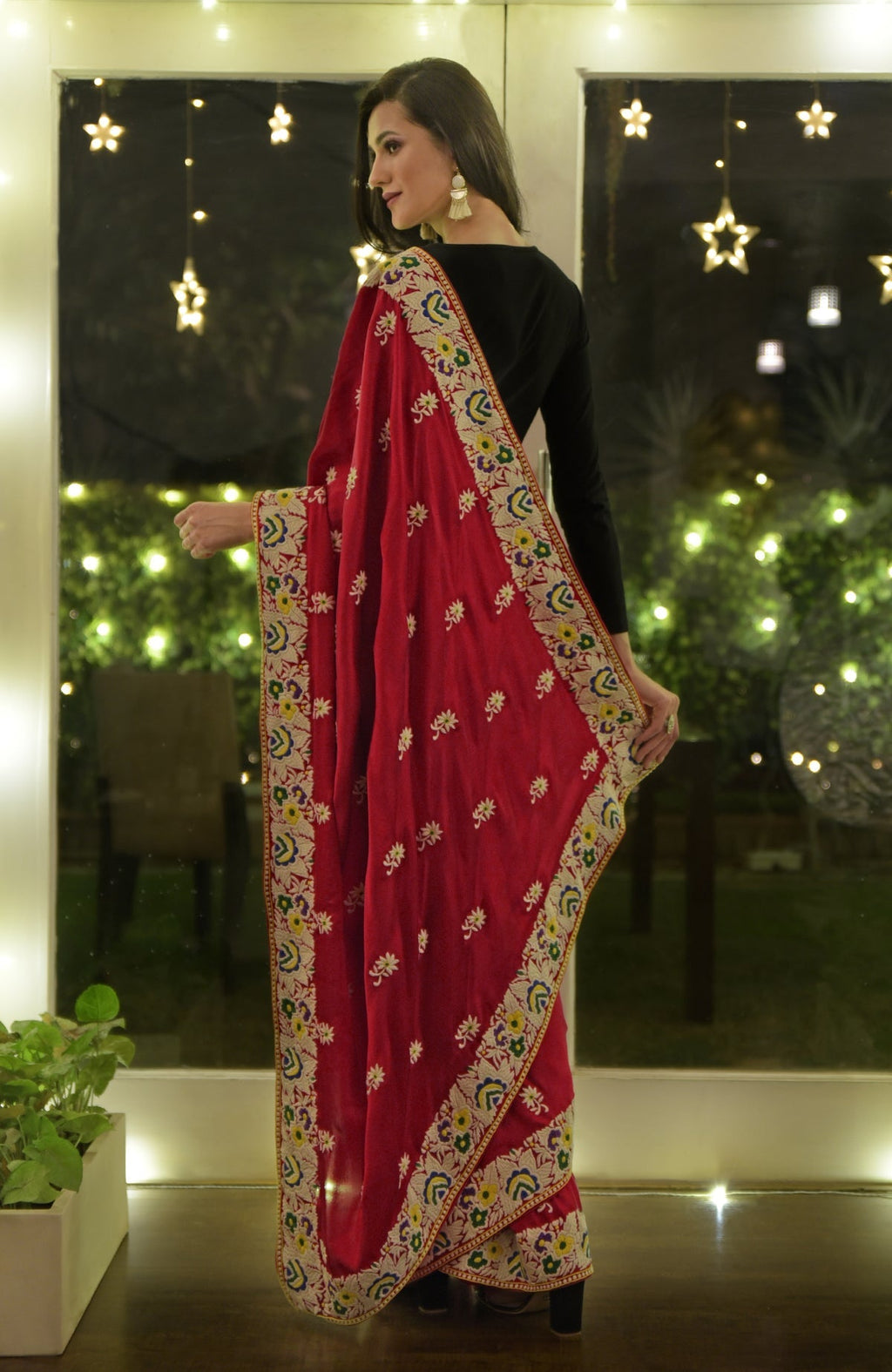 A woman models a red Parsi Gara hand-embroidered saree with a black blouse.