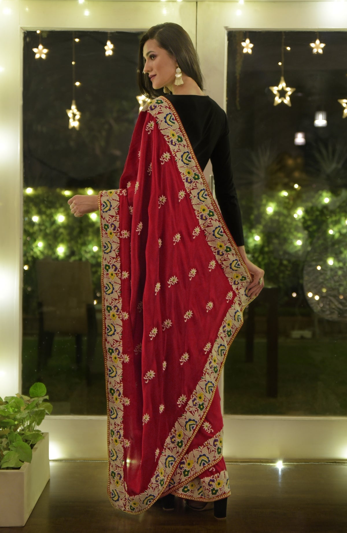 A woman models a red Parsi Gara hand-embroidered saree with a black blouse.