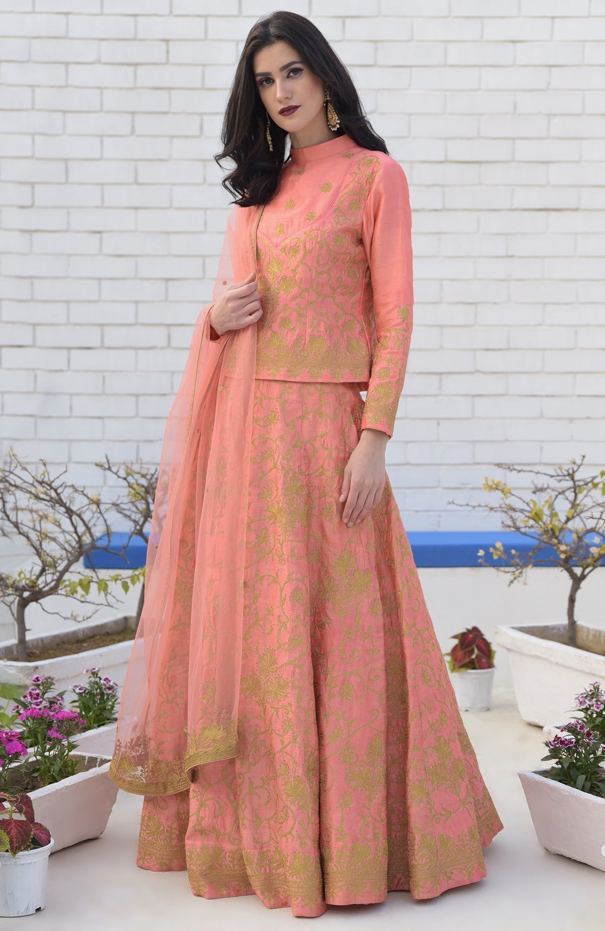 A woman models a peach lehenga set with gold embroidery and a sheer dupatta.