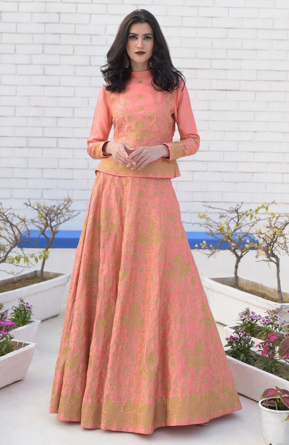 A woman models a peach lehenga set with gold Kashmiri tilla aari embroidery.