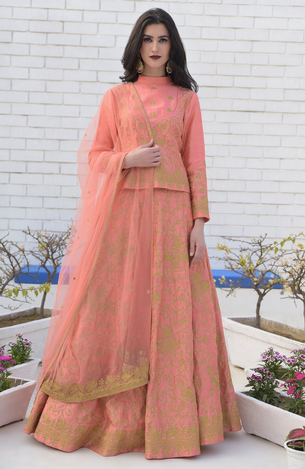 A woman models a peach lehenga set with gold embroidery and a sheer dupatta.