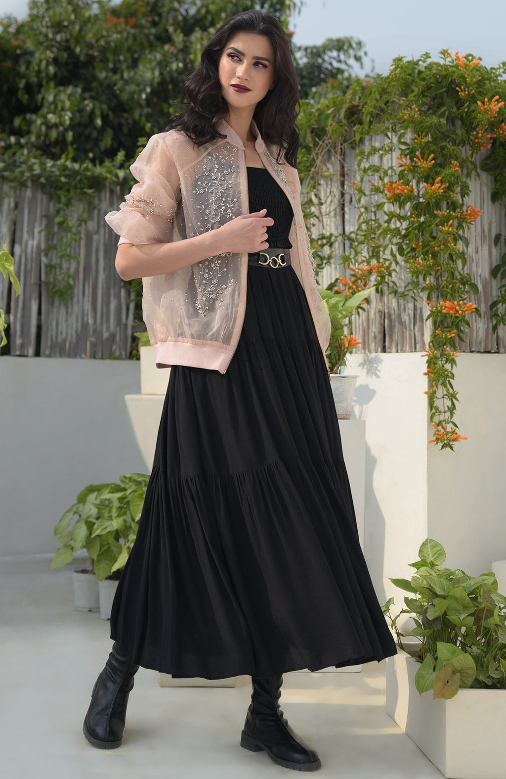 A woman wears a peach organza bomber jacket with crystal floweret embroidery over a black dress.