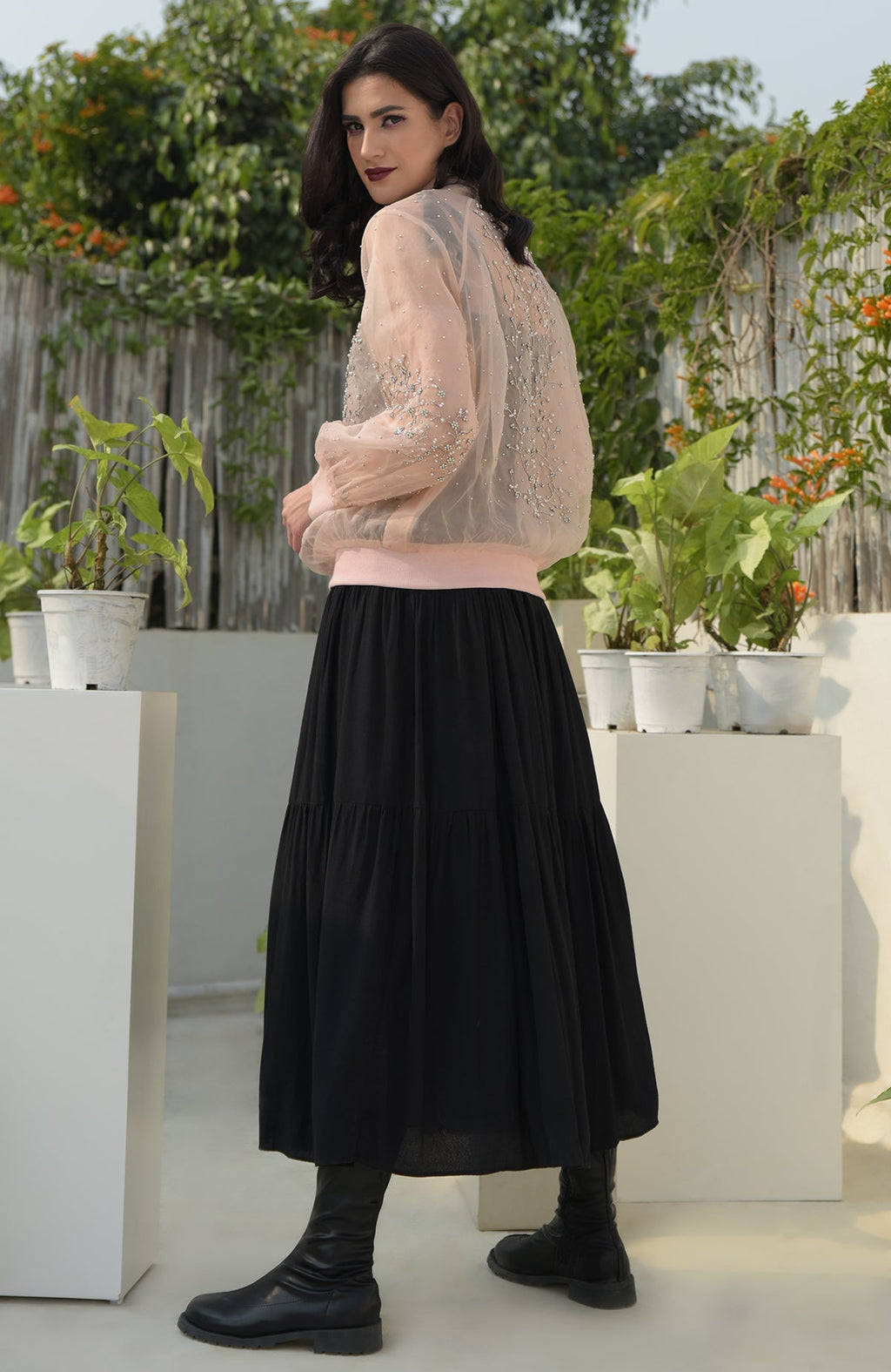 A woman models a peach organza bomber jacket with crystal flower embroidery and a black skirt.