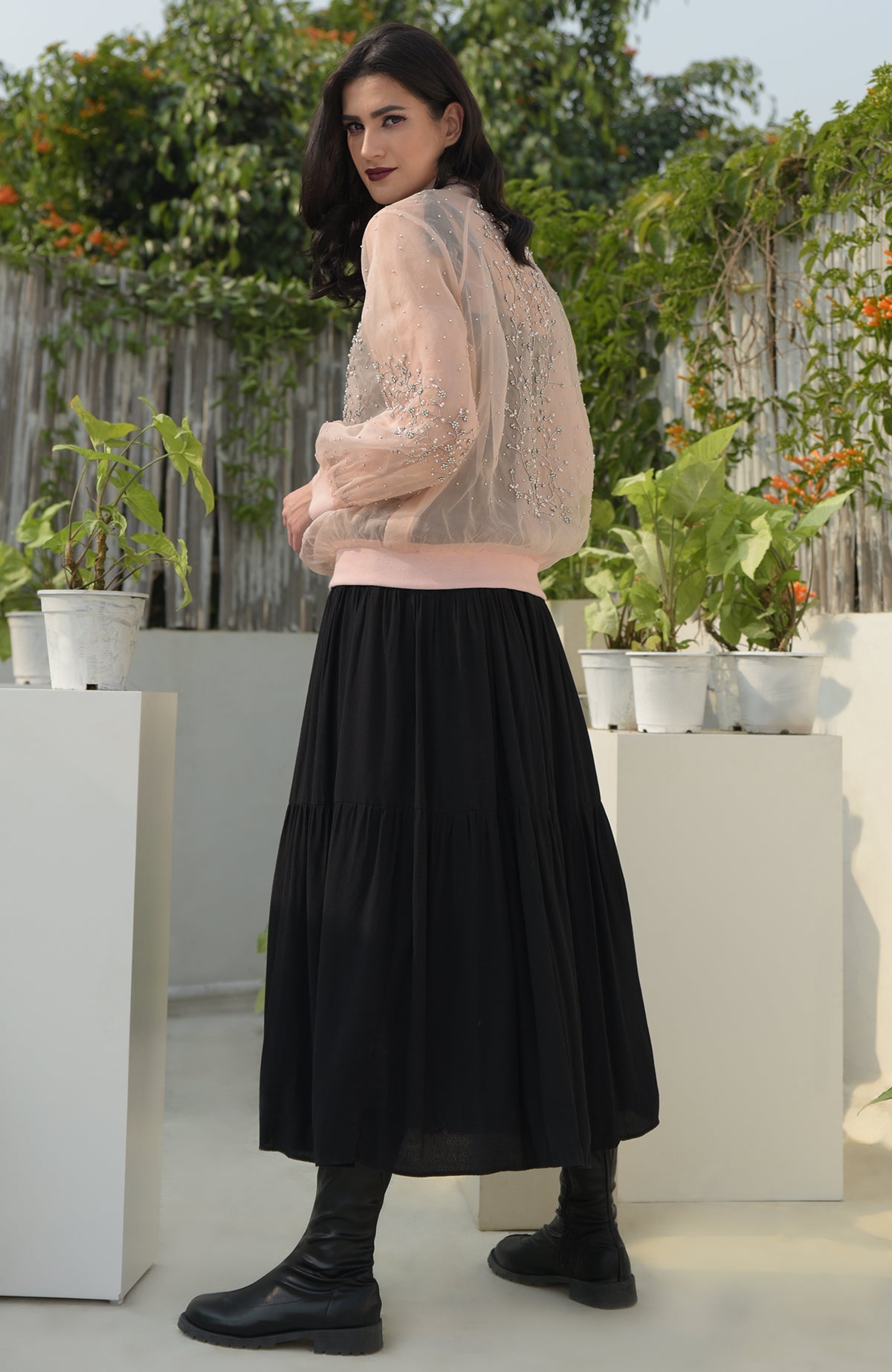 A woman models a peach organza bomber jacket with crystal flower embroidery and a black skirt.