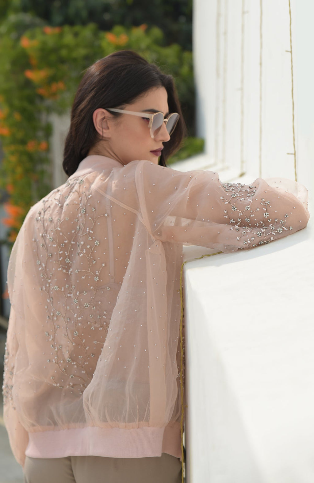 A woman models a peach organza bomber jacket with crystal floweret hand embroidery.