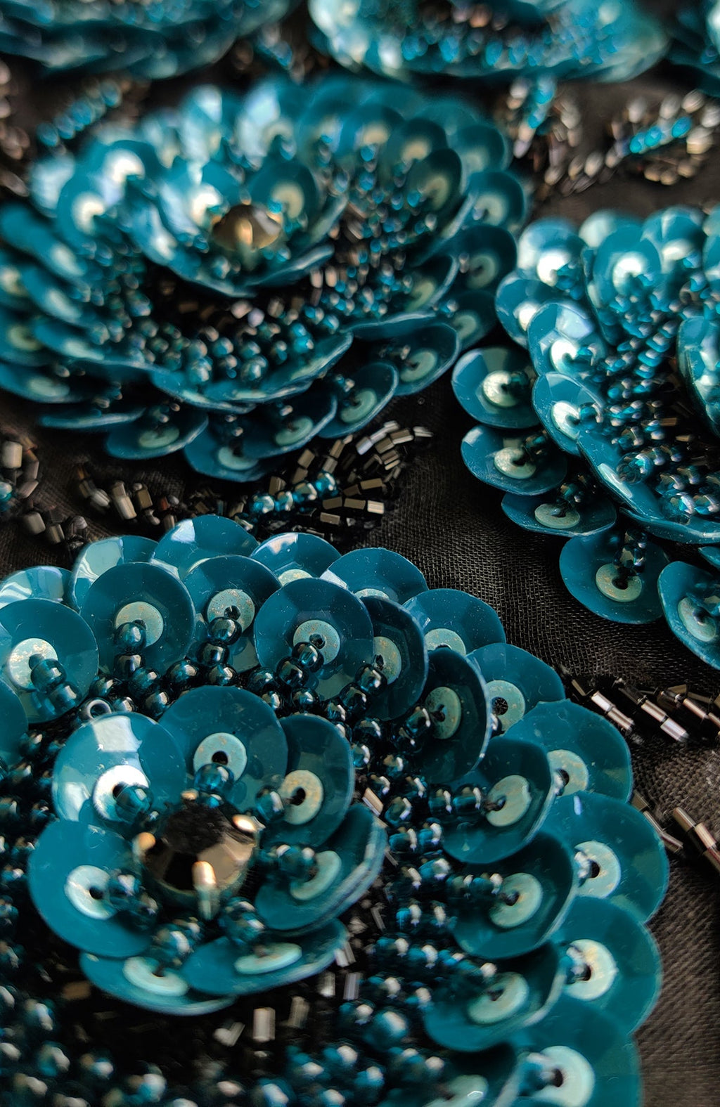 Close-up of blue sequin and bead floral embroidery on black fabric.