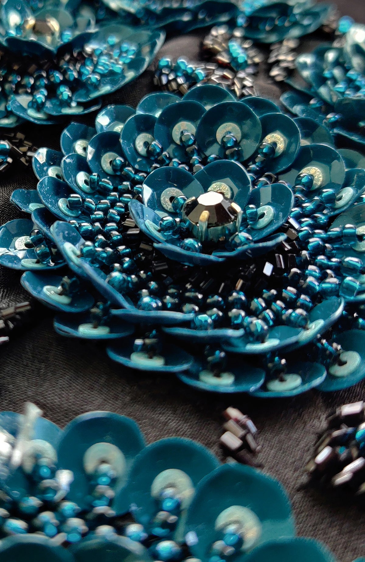 Close-up of blue 3D floral hand embroidery with sequins and beads on black fabric.