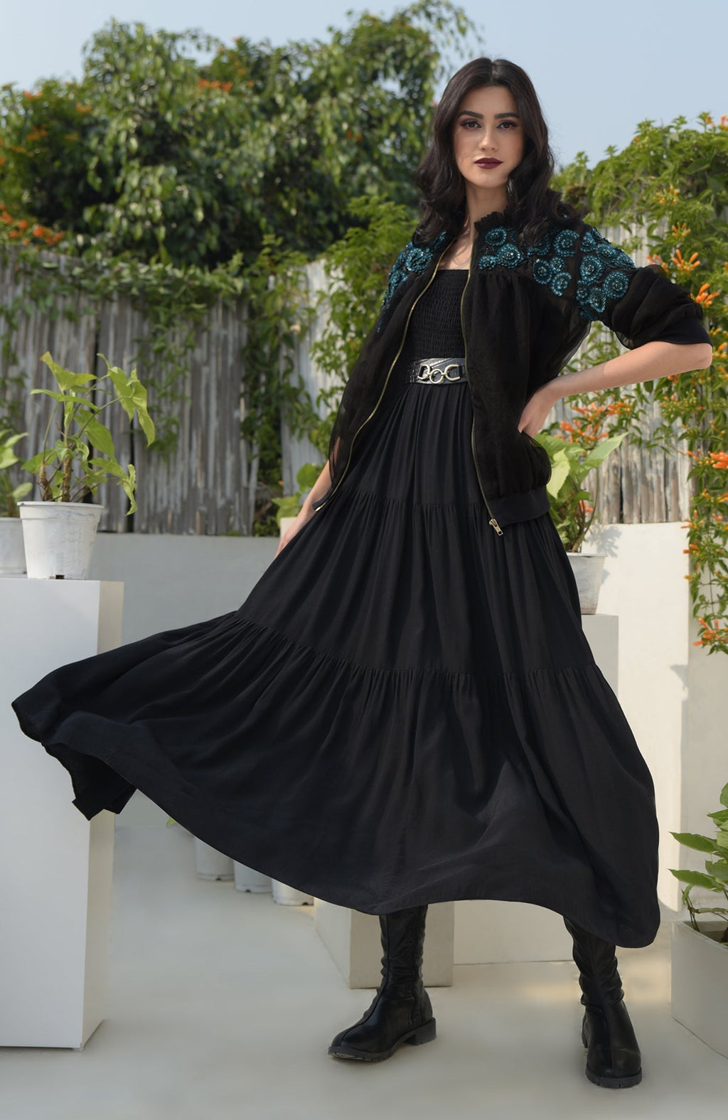A woman in a black bomber jacket with blue floral embroidery and a black dress.