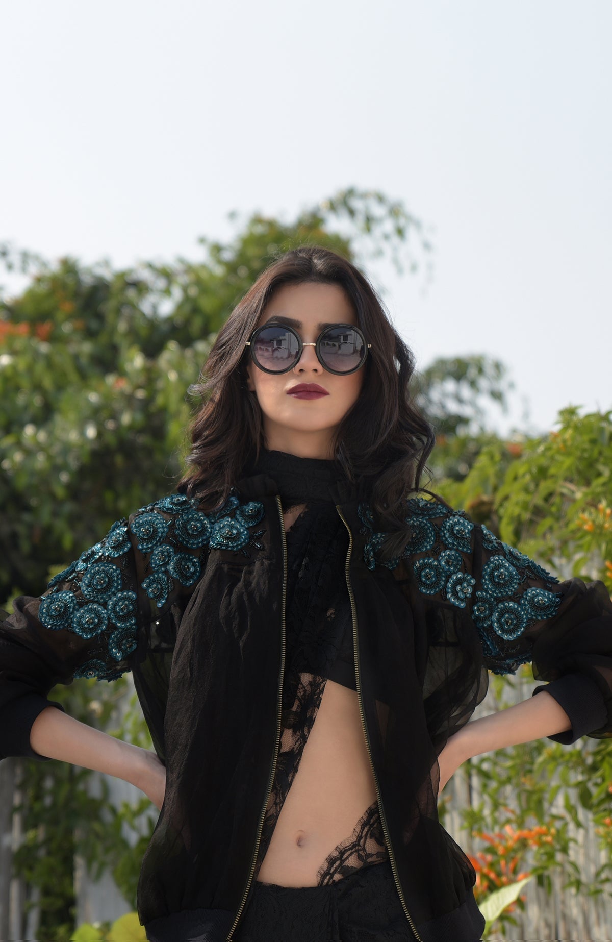 A woman models a black organza bomber jacket with blue 3D floral embroidery.