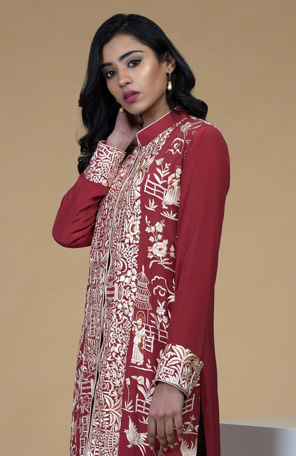 Shiraz red Parsi Gara embroidered jacket with beige, orange, and lilac Cheena Cheeni motifs and beige pants.