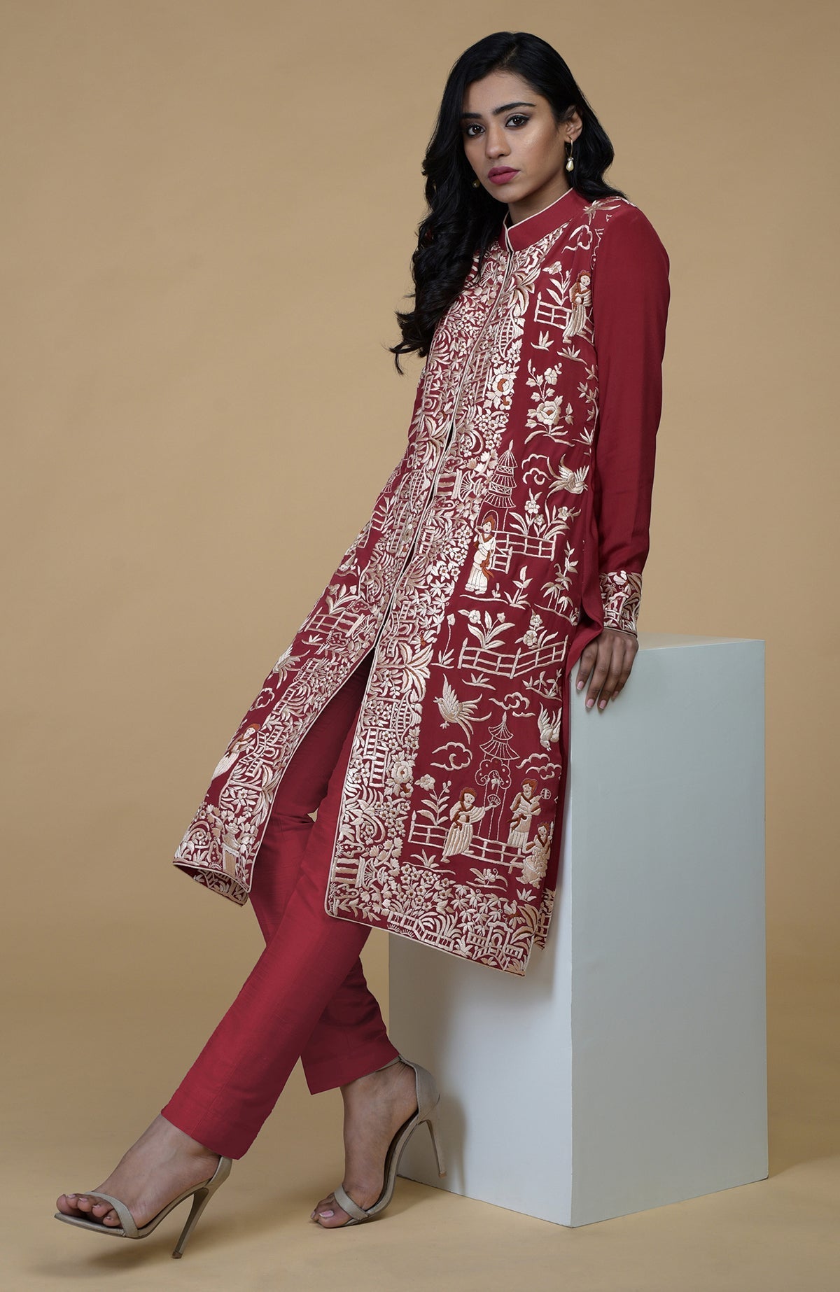 Shiraz red Parsi Gara embroidered jacket with beige, orange, and lilac Cheena Cheeni motifs and beige pants.