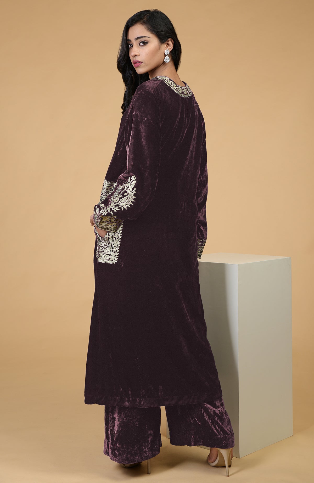 A woman models a mulled wine velvet kurta set with Kashmiri tilla embroidery.