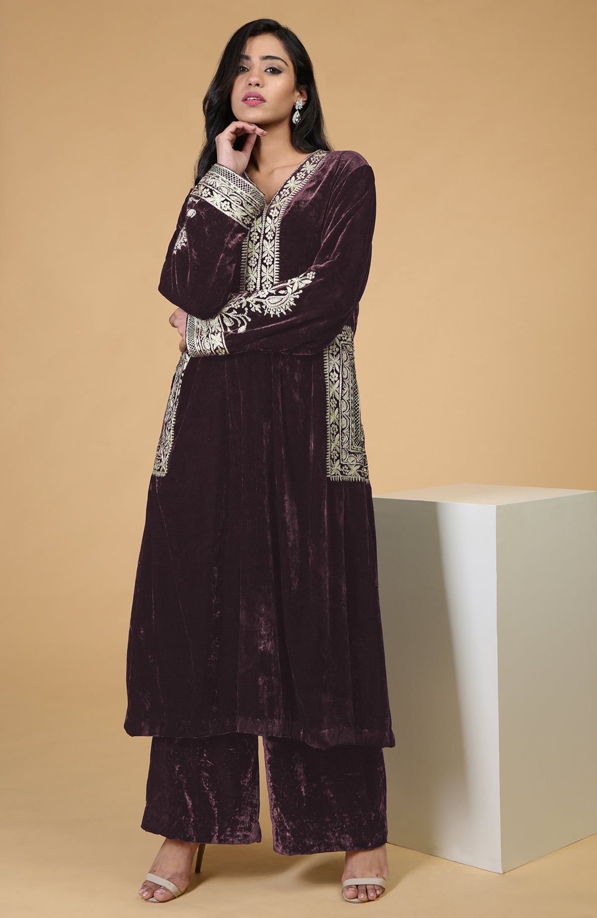 A woman models a dark purple velvet kurta set with gold embroidery.