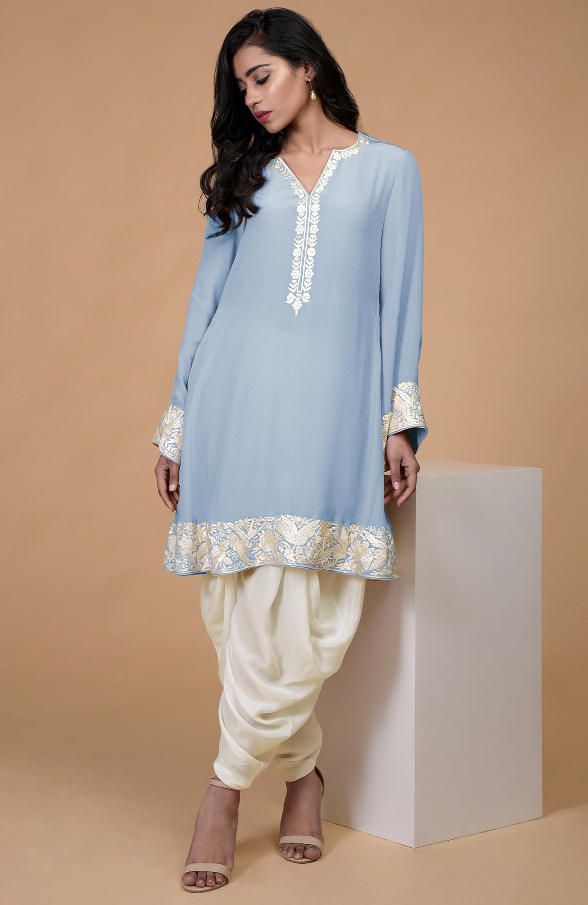 A woman models a light blue Parsi Gara embroidered kurta with ivory cowl patiala pants.