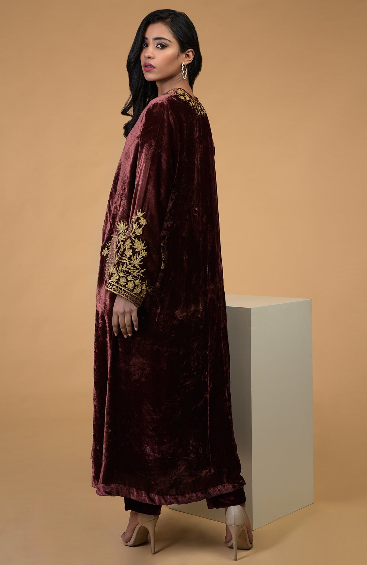 A woman models a rusty rose velvet choga kurta set with gold embroidery.