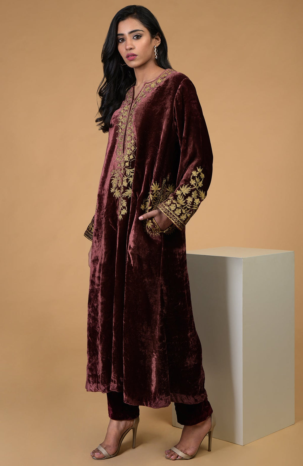 A woman models a rusty rose velvet kurta set with gold embroidery.