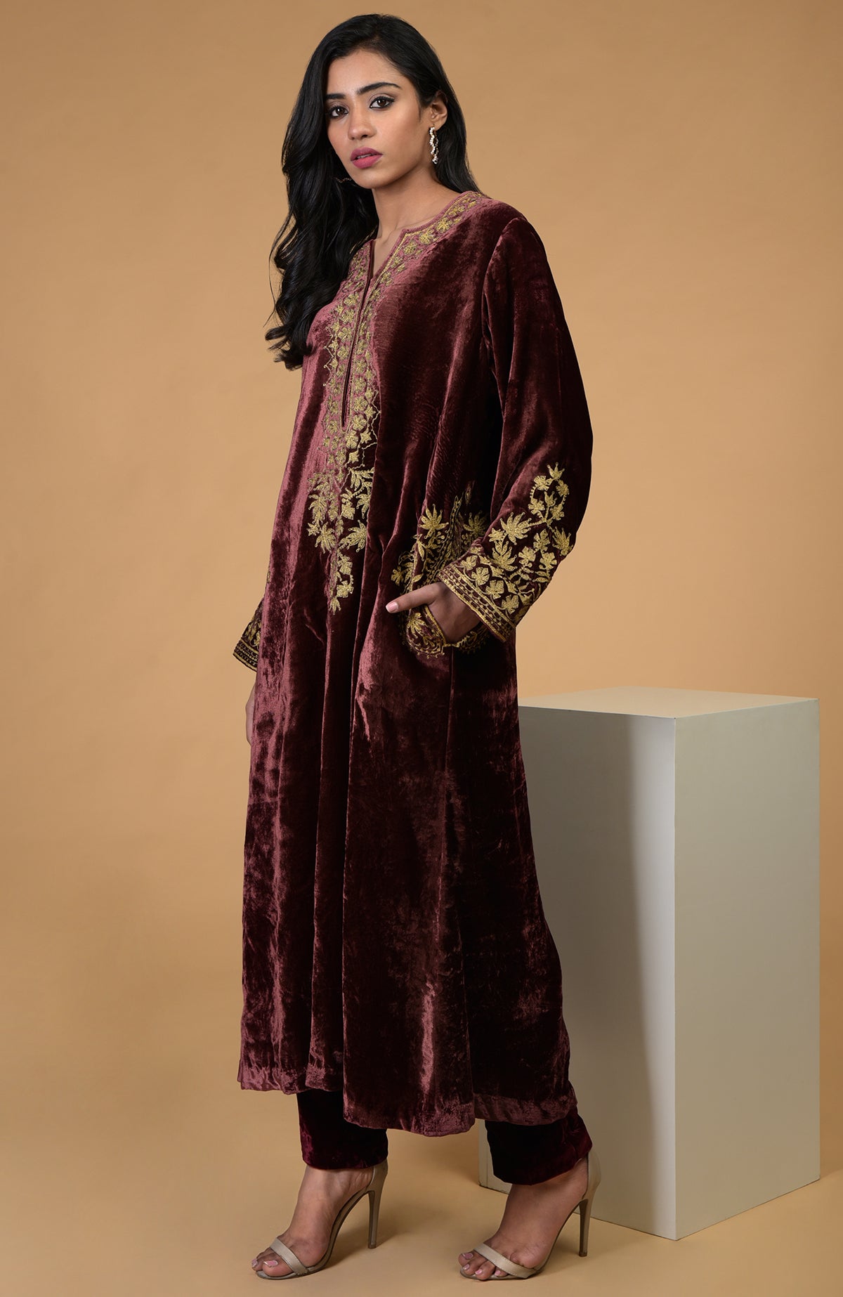 A woman models a rusty rose velvet kurta set with gold embroidery.