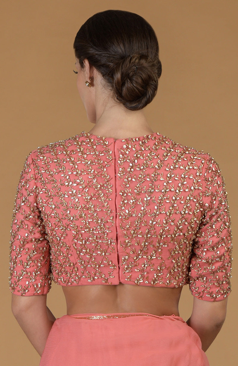 A woman from behind wears a salmon pink blouse with gold embroidery and a matching saree.