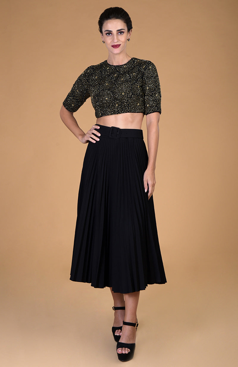 Black gold hand embroidered blouse with a black pleated skirt and black heels.