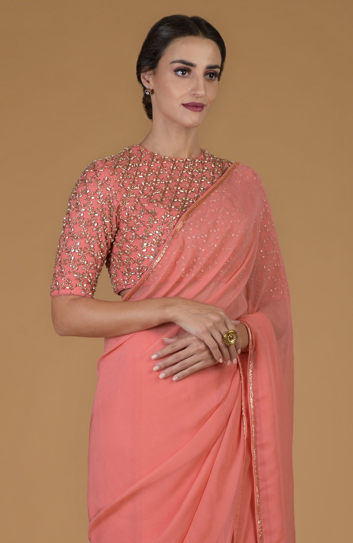 A woman models a salmon pink saree with a heavily embroidered blouse.