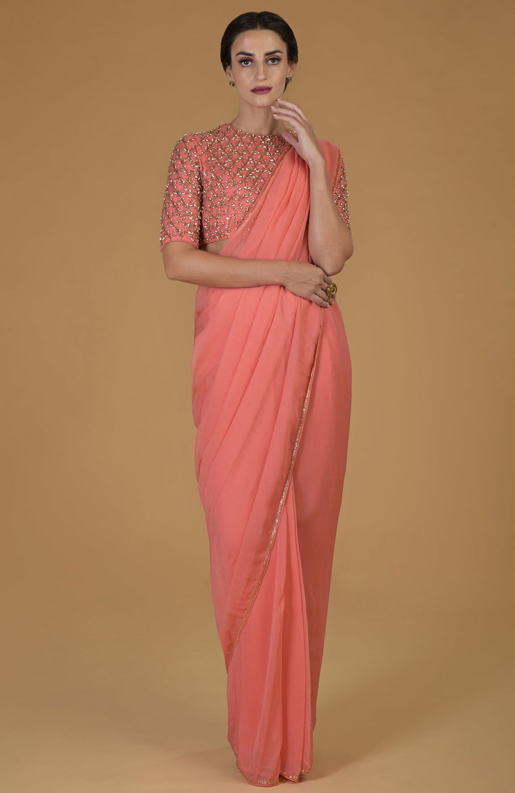 Woman in a salmon pink saree with a matching embroidered blouse.