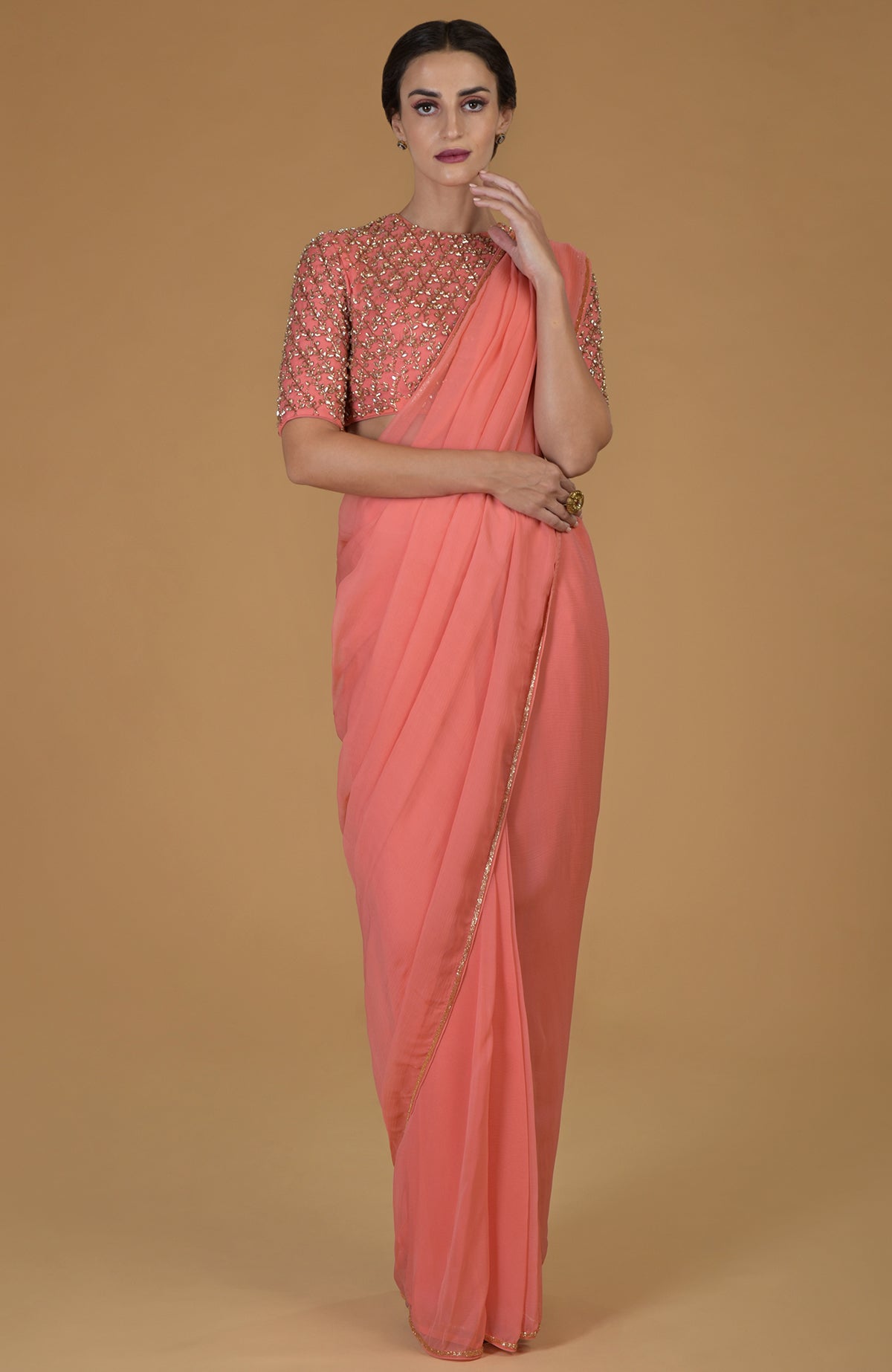 Woman in a salmon pink saree with a matching embroidered blouse.