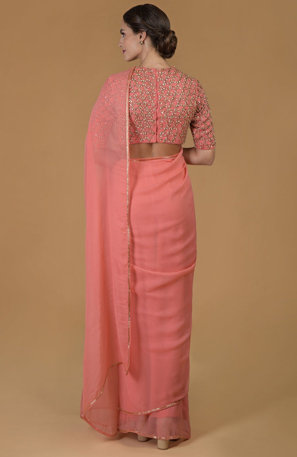 A woman from behind wears a salmon hand-embroidered saree and blouse.