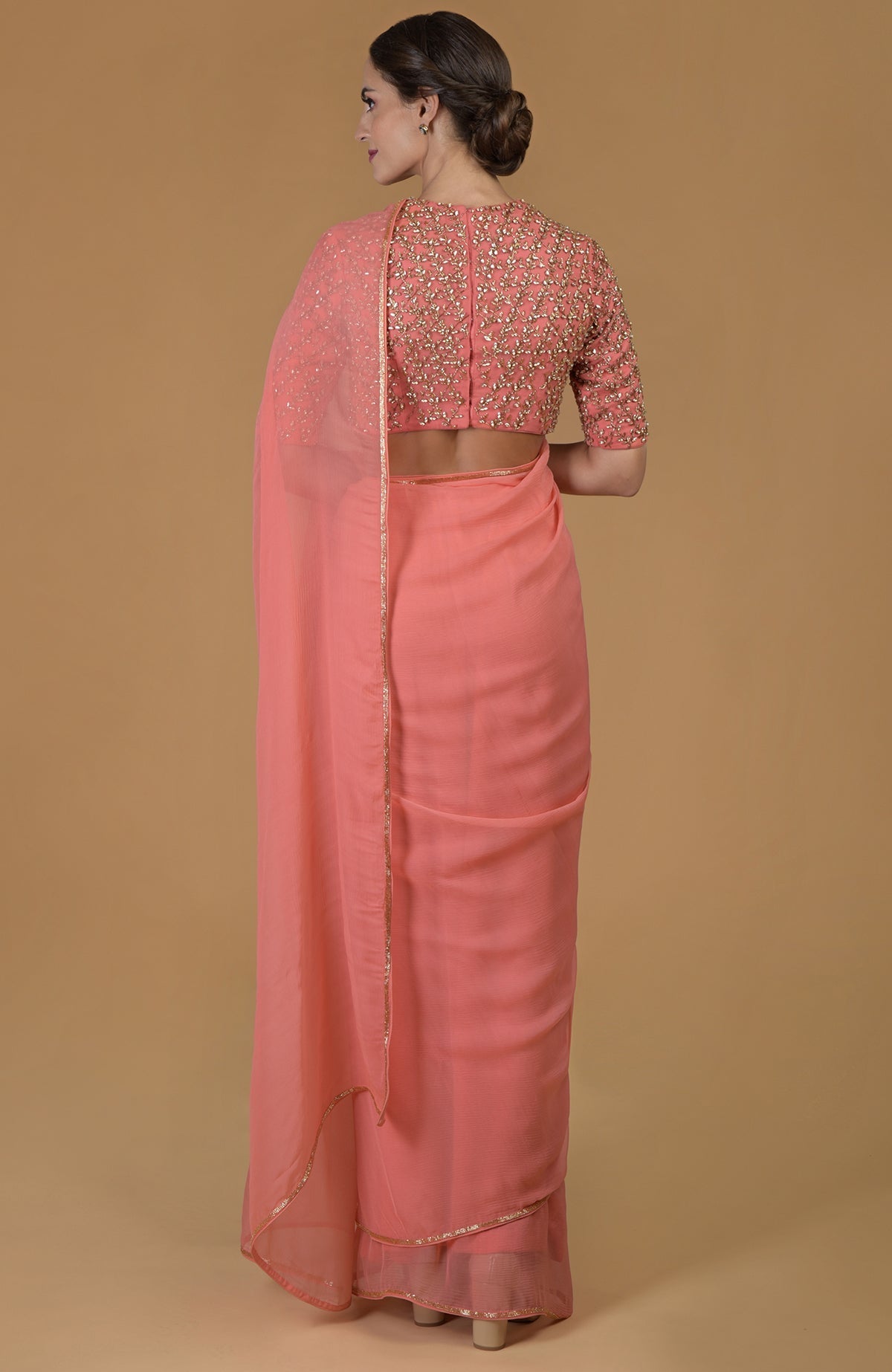 A woman from behind wears a salmon hand-embroidered saree and blouse.