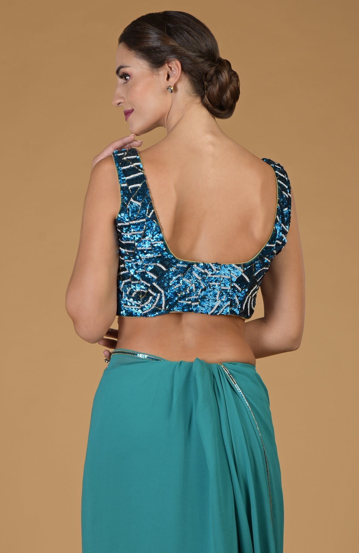 A woman models a blue sequined blouse and a teal saree with a beaded waistline.