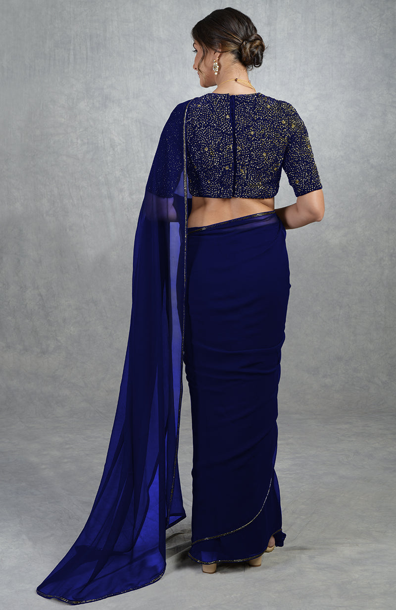 A woman from behind wears a royal blue saree with a gold embroidered blouse.