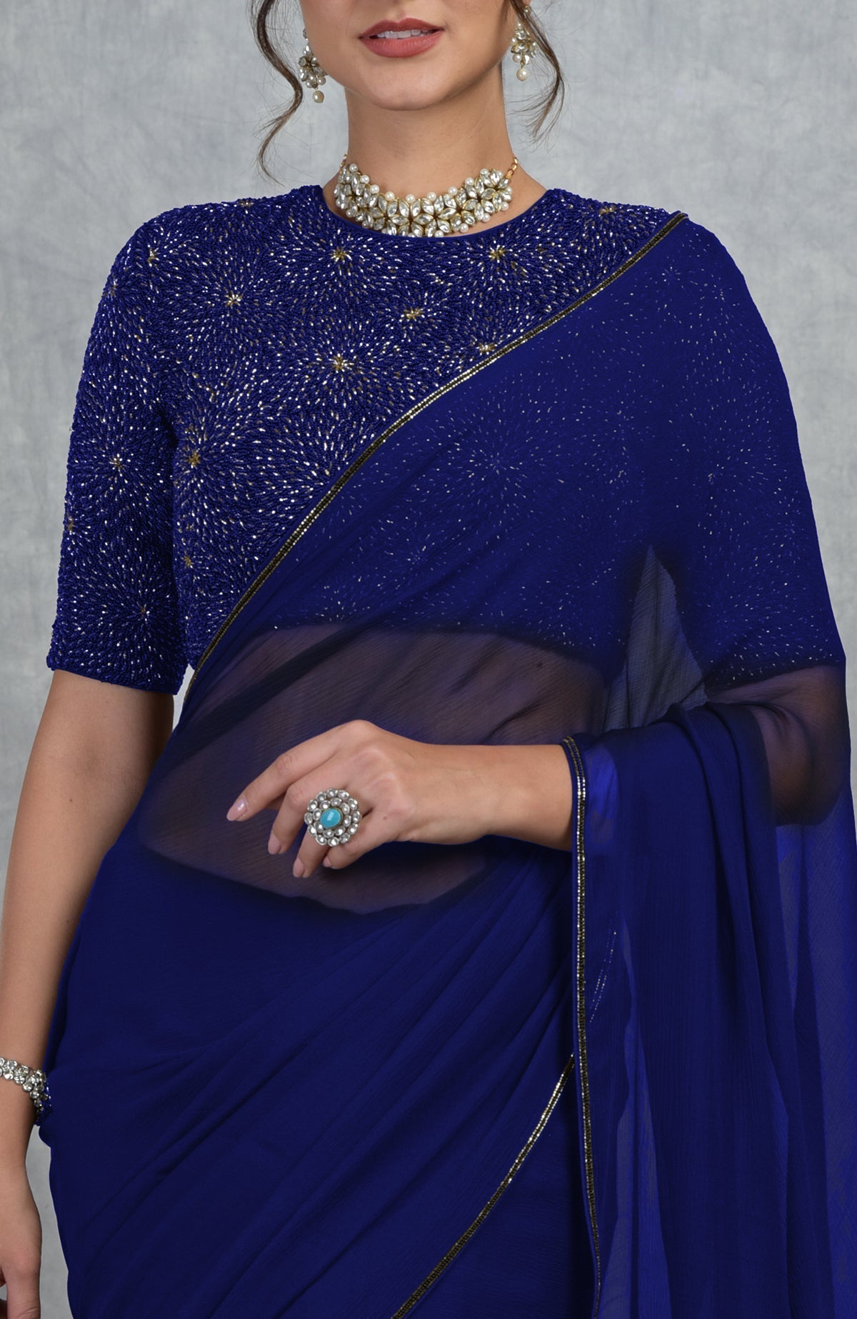 A woman models a royal blue chiffon saree with a gold hand-embroidered blouse.