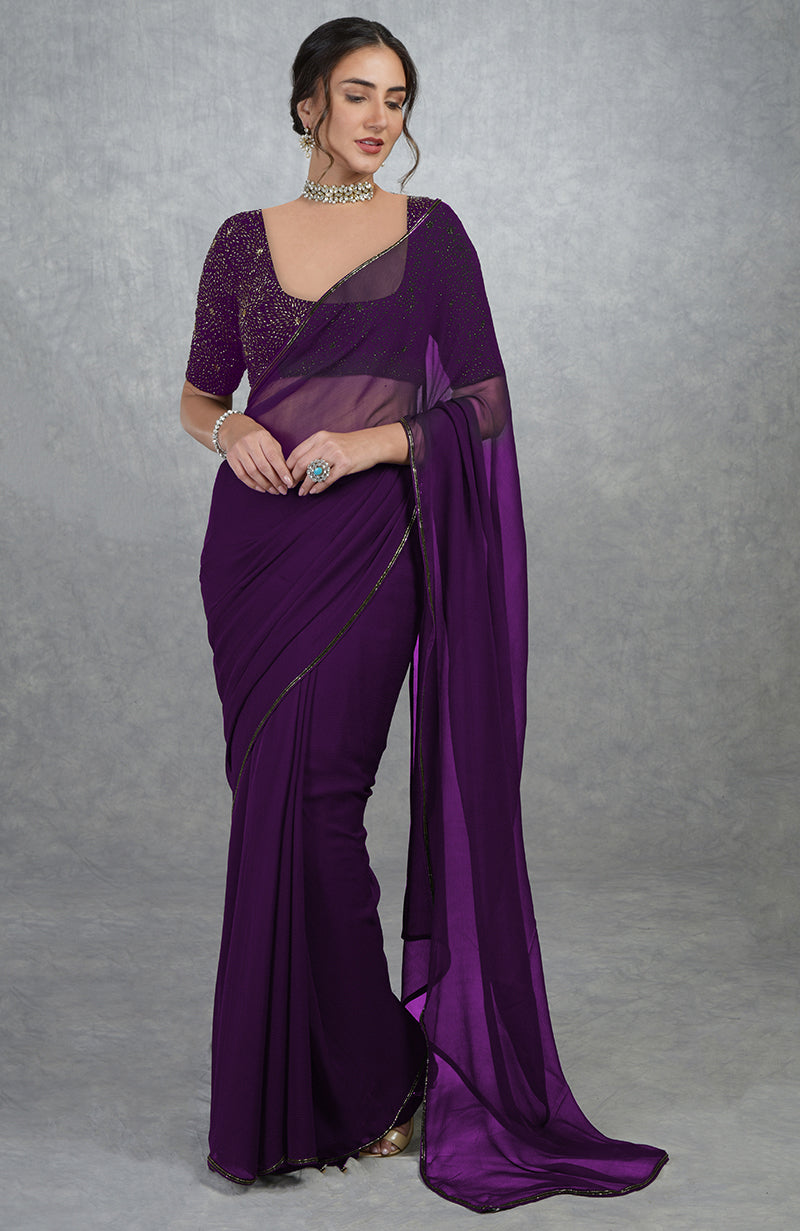 A woman models a purple saree with a sheer, embroidered blouse.