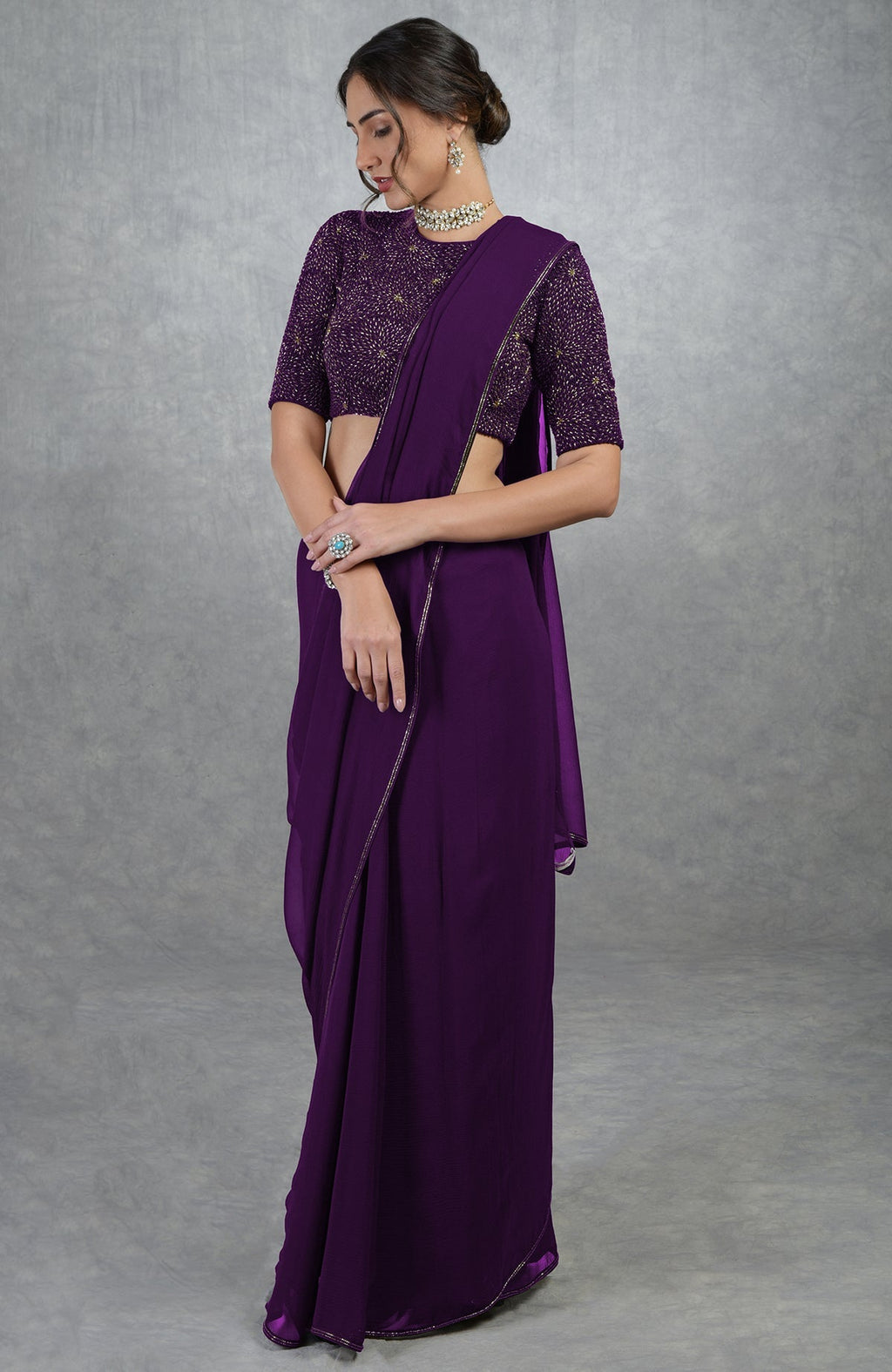 A woman models a plum purple gold hand-embroidered saree and blouse.