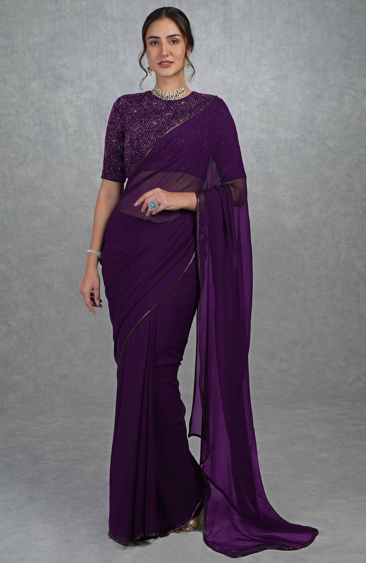 A woman models a plum purple gold hand-embroidered saree and blouse.