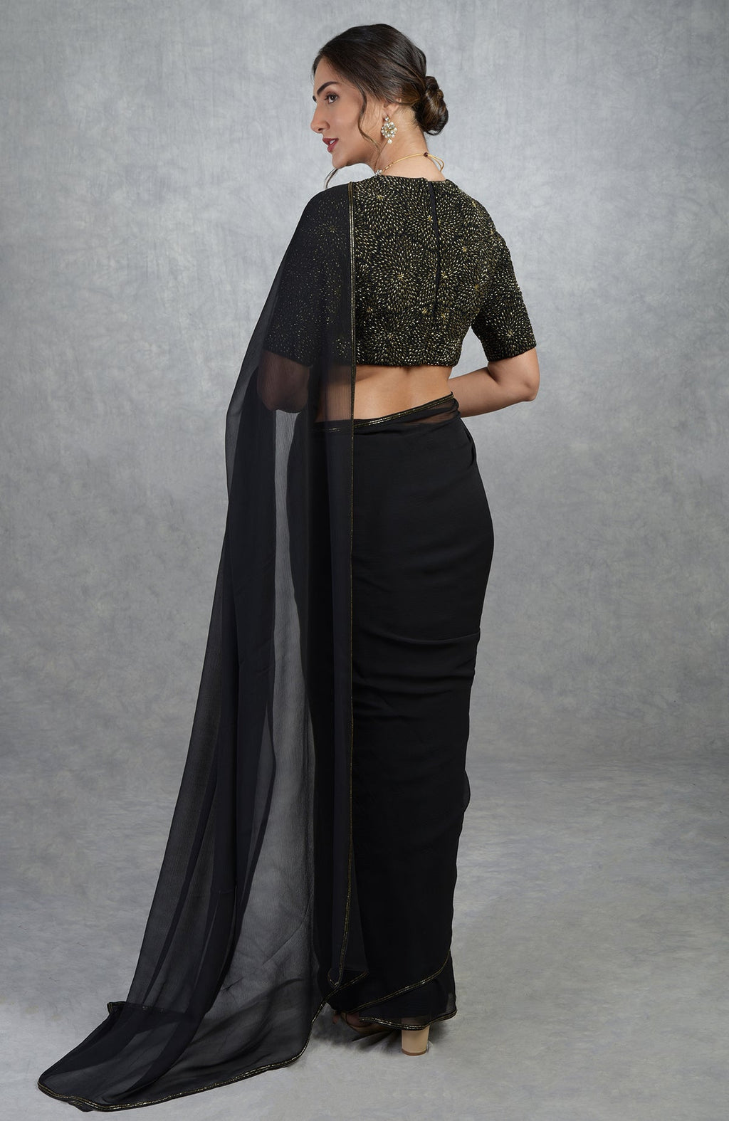 A woman from the back wearing a black and gold hand-embroidered saree and blouse.