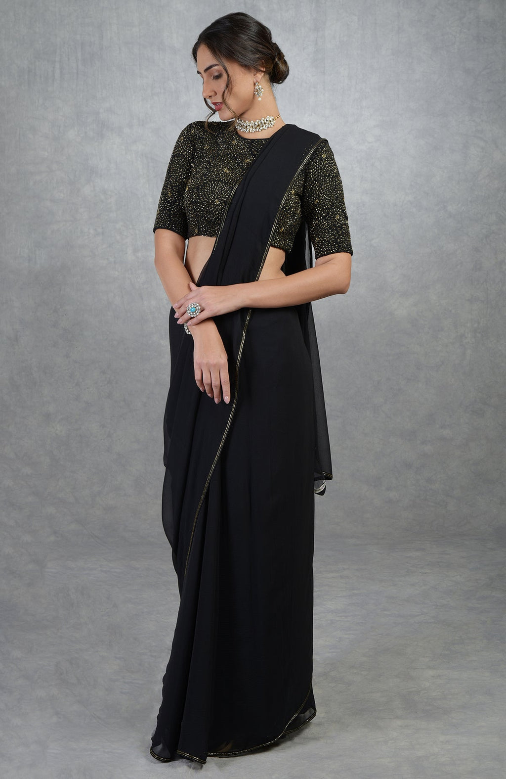 A woman in a black and gold hand-embroidered saree and blouse.