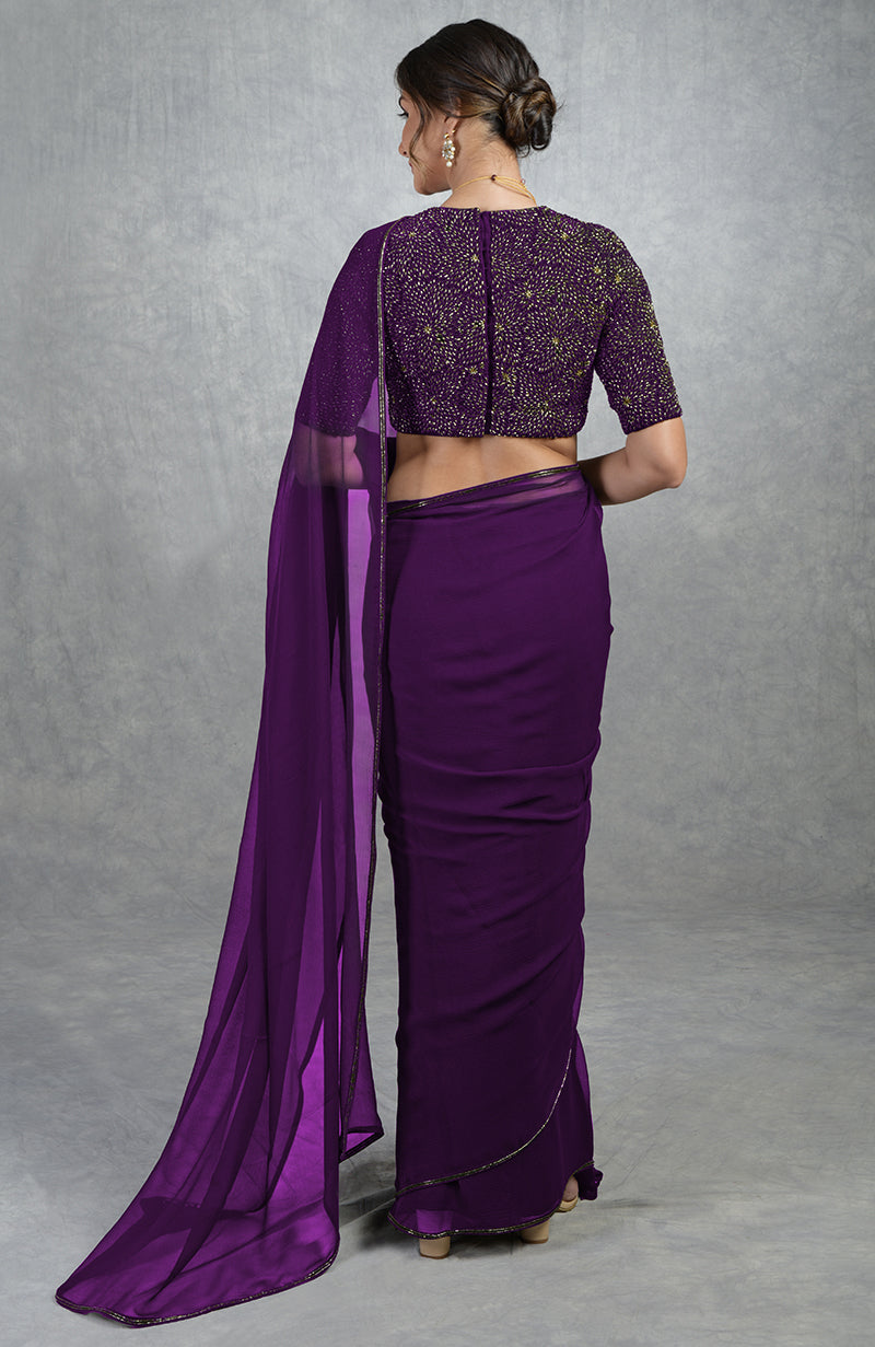 A woman from behind wears a plum purple saree with a gold embroidered blouse.