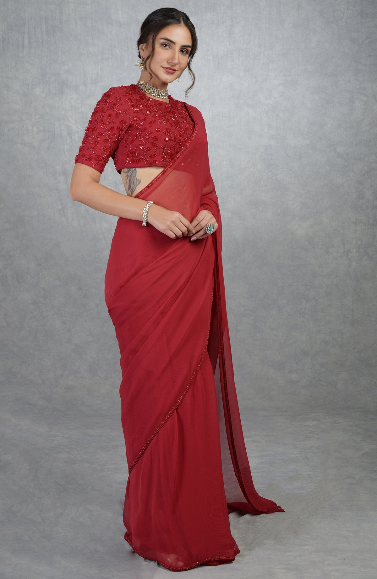 A woman models a red hand-embroidered saree and blouse with a choker and bracelet.