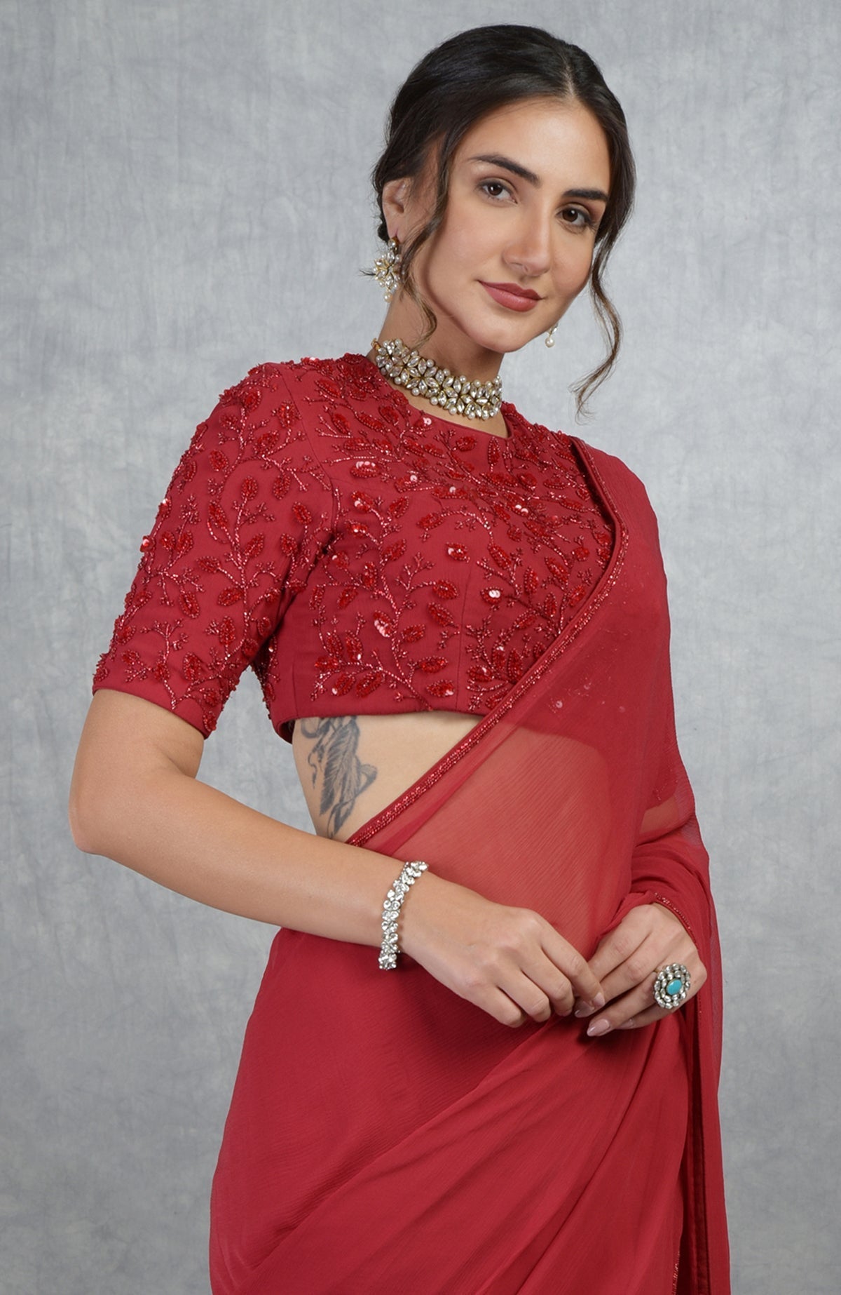 A woman in a red hand-embroidered saree and blouse with a choker necklace.