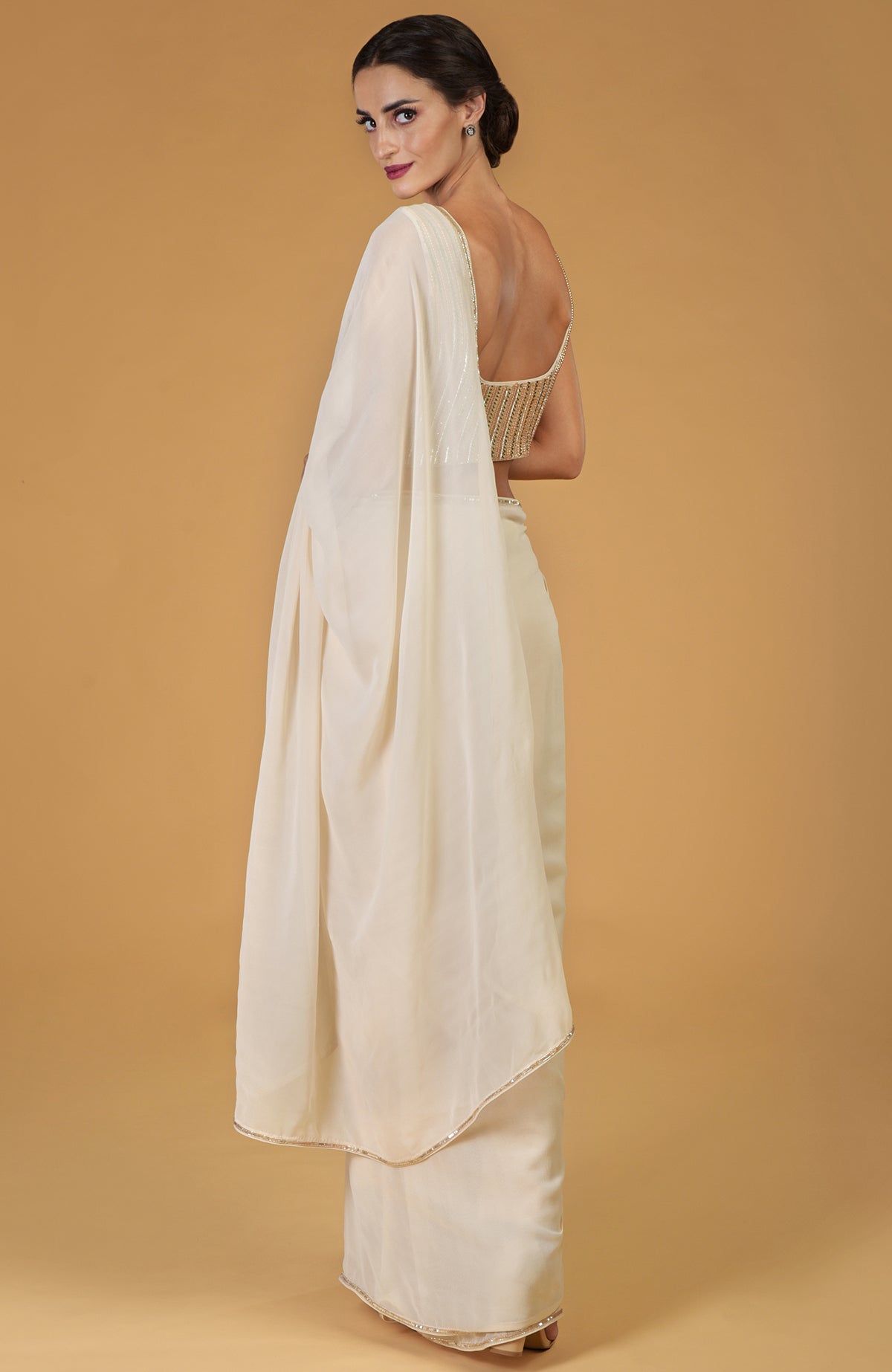 A woman models a champagne gold hand-embroidered saree and blouse.