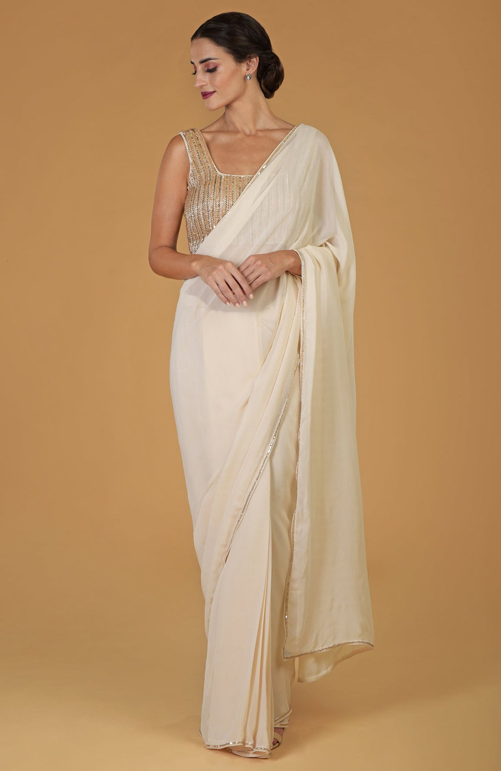 A woman models a champagne gold hand-embroidered saree and blouse.