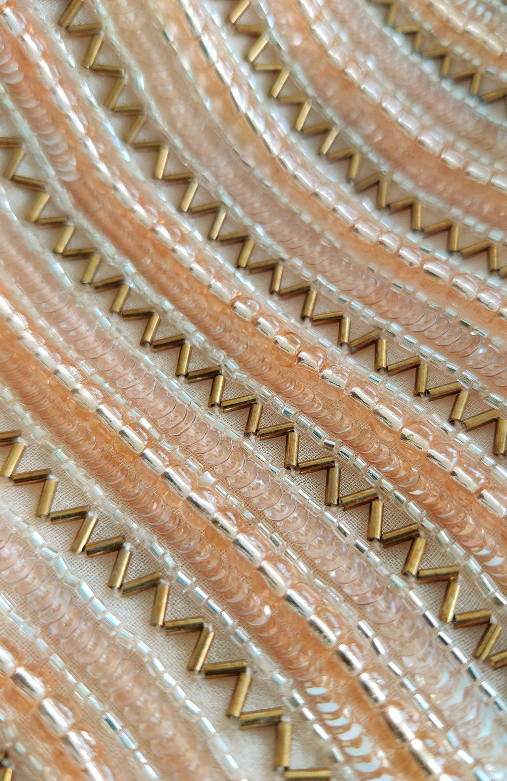 Close-up of champagne gold hand embroidery with beads and sequins in a zig-zag pattern.