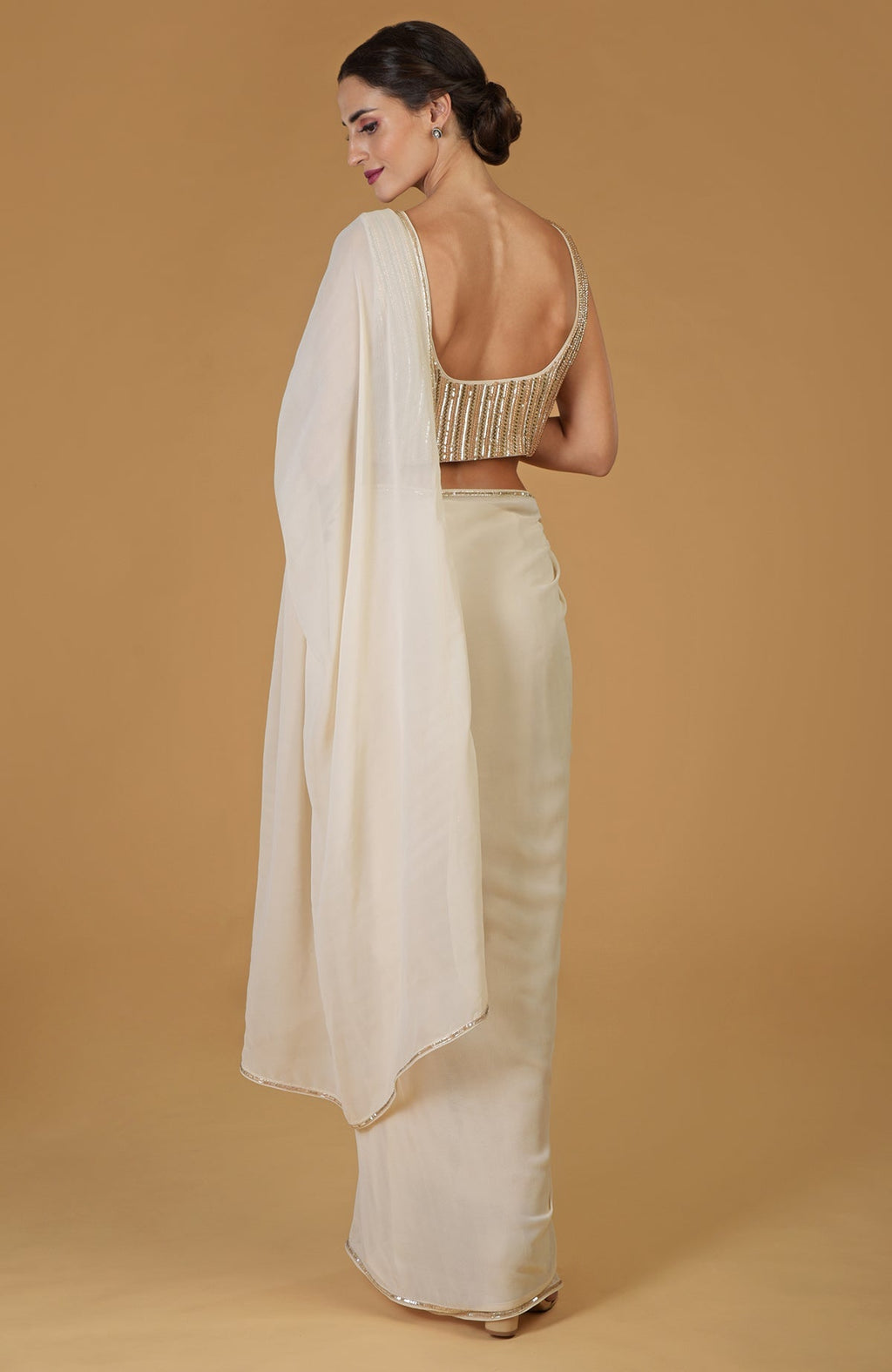 A woman models a champagne gold hand-embroidered saree and blouse.