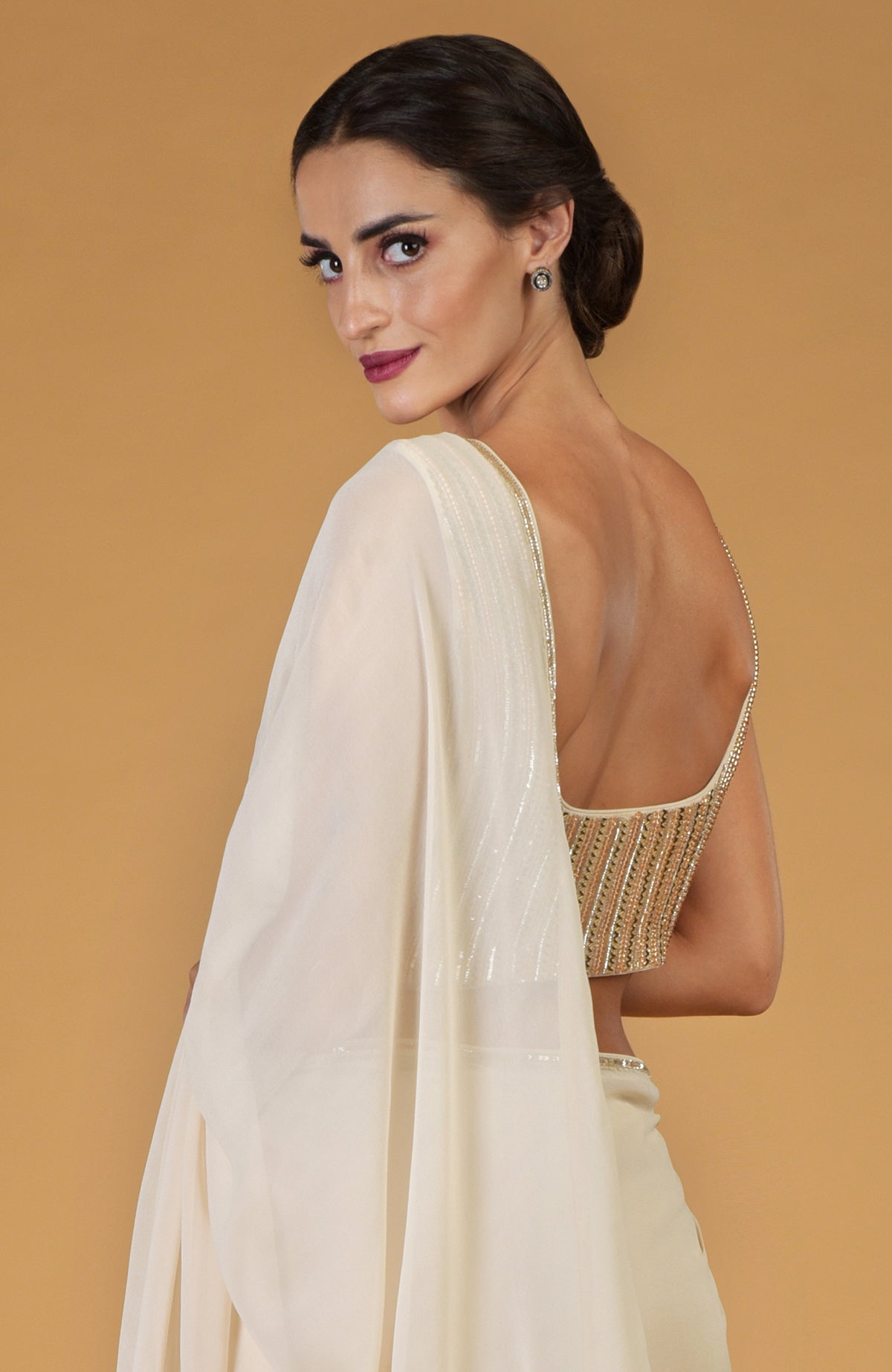 A woman in a champagne gold hand-embroidered saree and blouse looks over her shoulder.